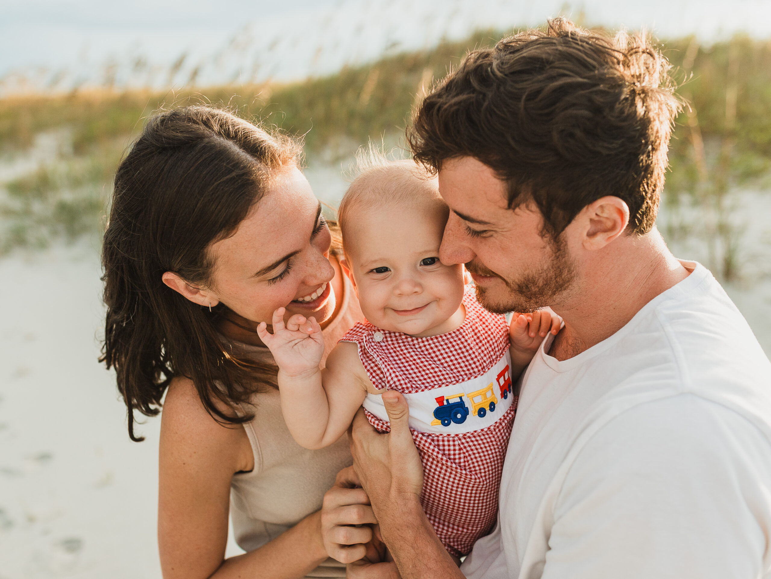 Father, mother, and baby posing for a family photo at the beach.