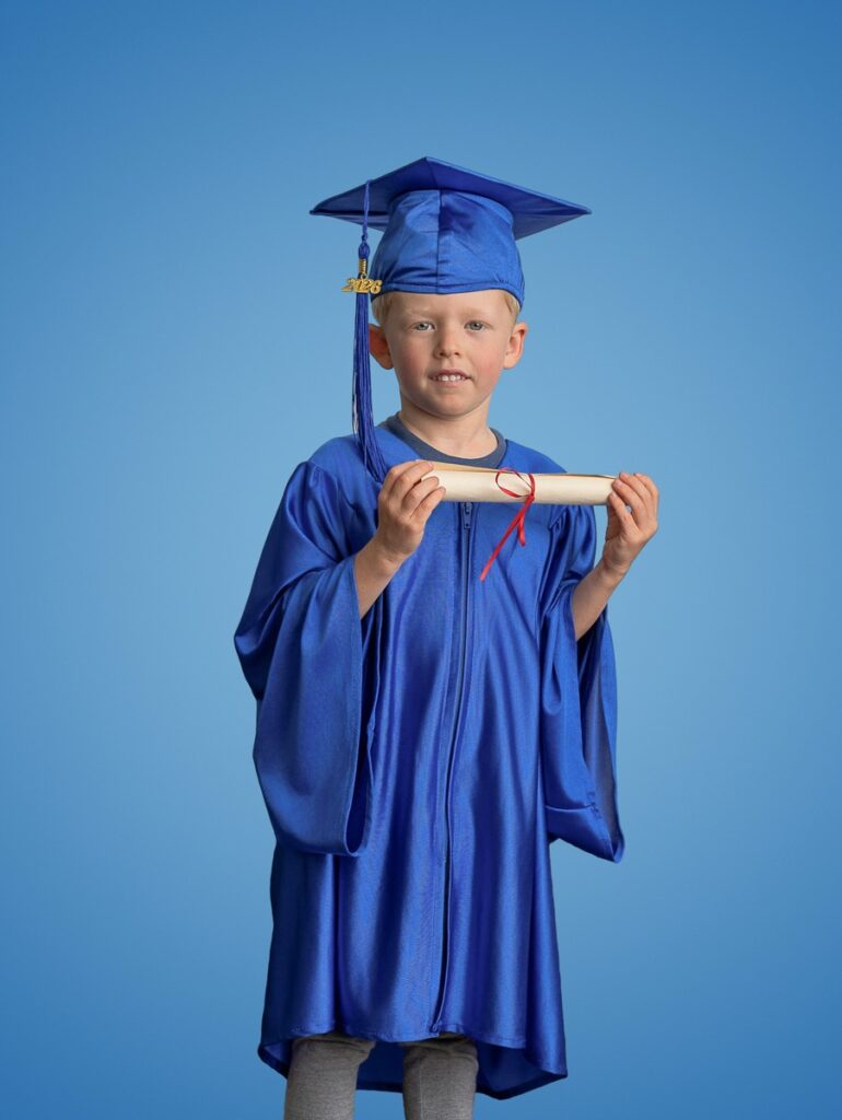 Cap and gown preschool graduation portrait of a boy wearing a blue robe  cap and with a gold tassel holding a diploma proudly.